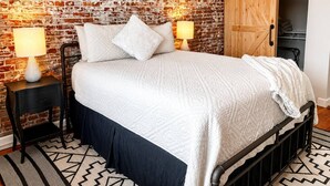A bedroom with a brick wall, a wooden wardrobe, a bed with a white quilt, two bedside tables with lamps, and a patterned rug. - Suite Victory #7 On Main St w/Reserved Parking (Galena)