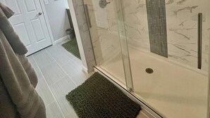 A modern bathroom with a glass-enclosed shower, a white door, and a green rug on the floor. - Suite Victory #7 On Main St w/Reserved Parking (Galena)