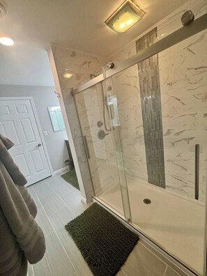 Un bagno moderno con cabina doccia in vetro, una porta bianca e un tappeto verde sul pavimento.