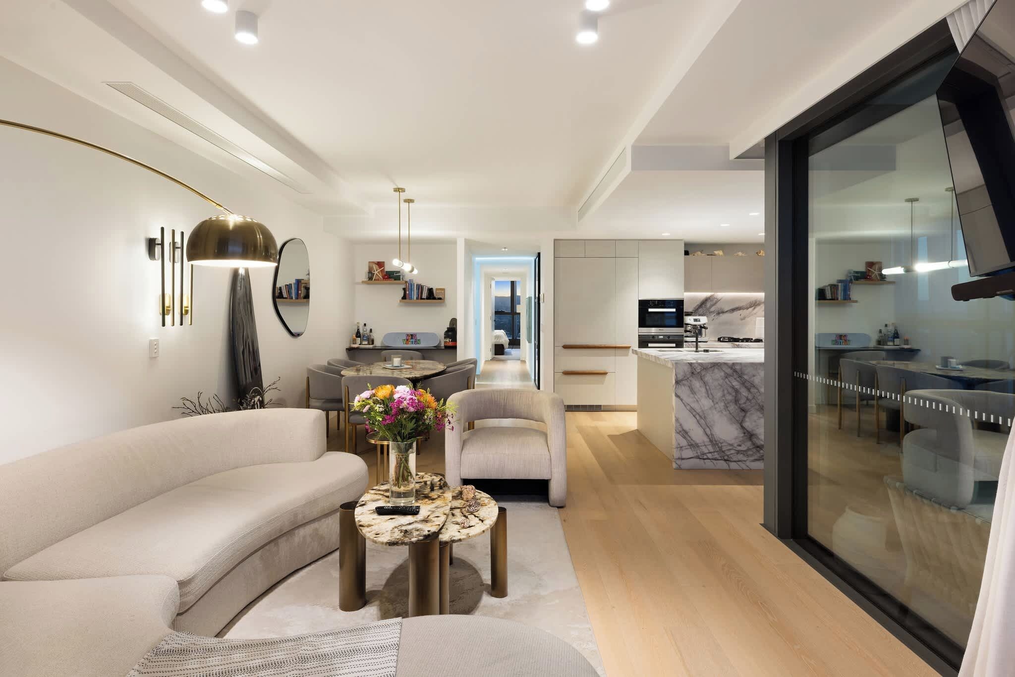 A modern living room with a sofa, a coffee table with flowers, and a dining area with chairs.
