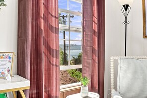 Une pièce avec vue sur un plan d’eau, une chaise blanche, une petite table avec une plante et un tableau encadré au mur.
