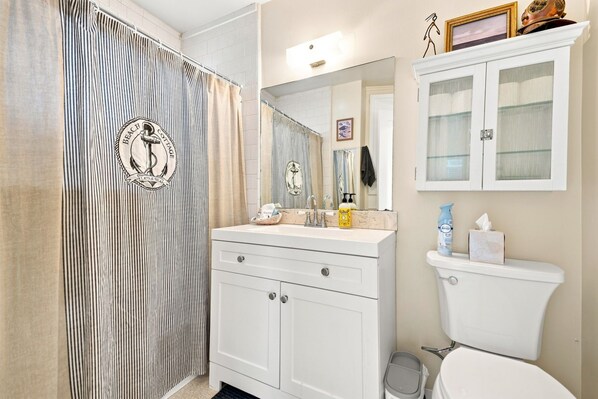 Une salle de bain avec un rideau de douche à rayures, un lavabo avec un miroir, des toilettes et un meuble au-dessus des toilettes.