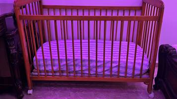 Una culla in legno con un materasso decorato, posizionata di fronte a una parete illuminata di viola.