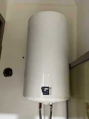A white water heater mounted on a wall with two visible pipes.