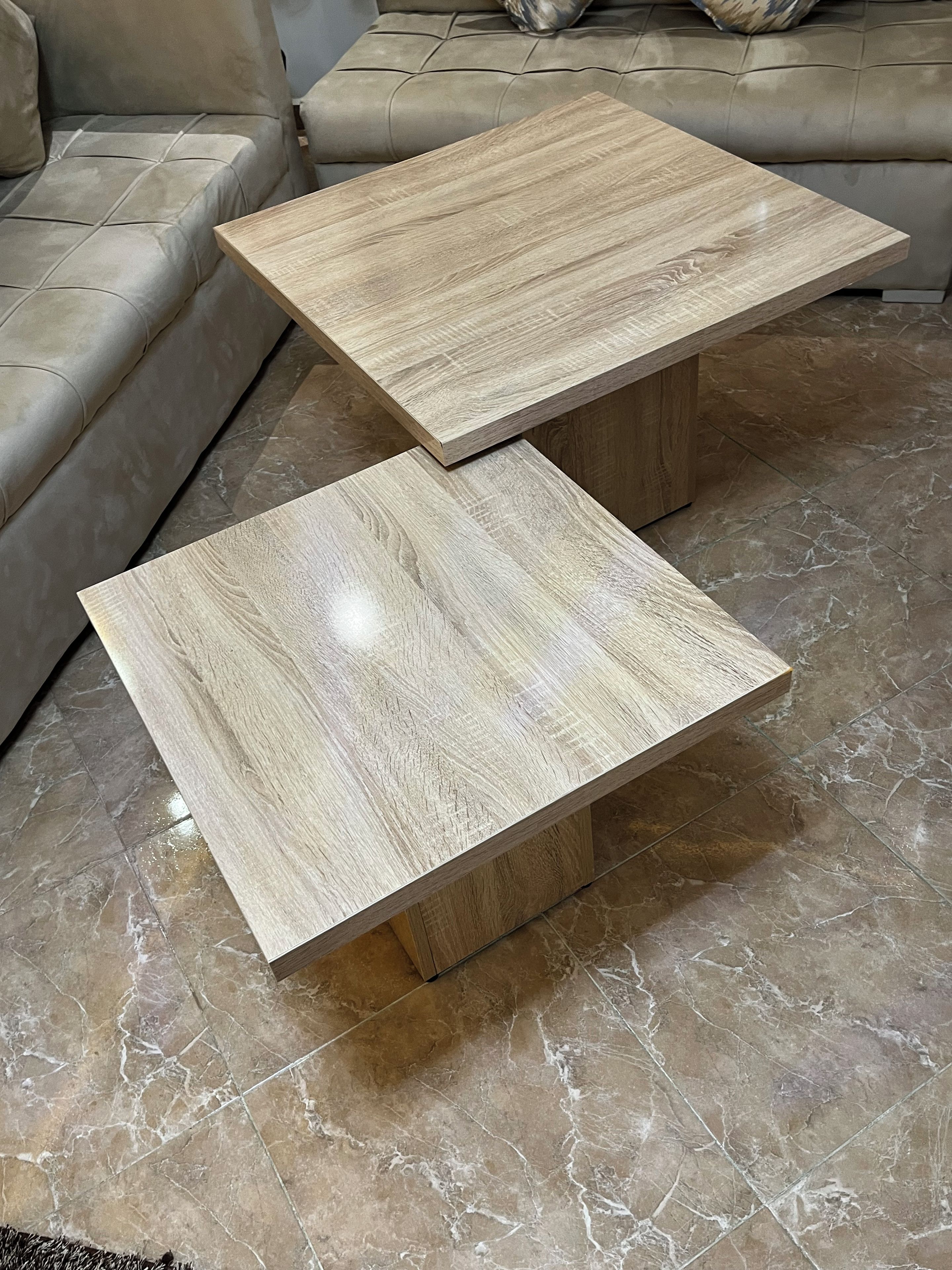 Dos mesas cuadradas de centro de madera con acabado en madera clara, sobre un piso de mármol.