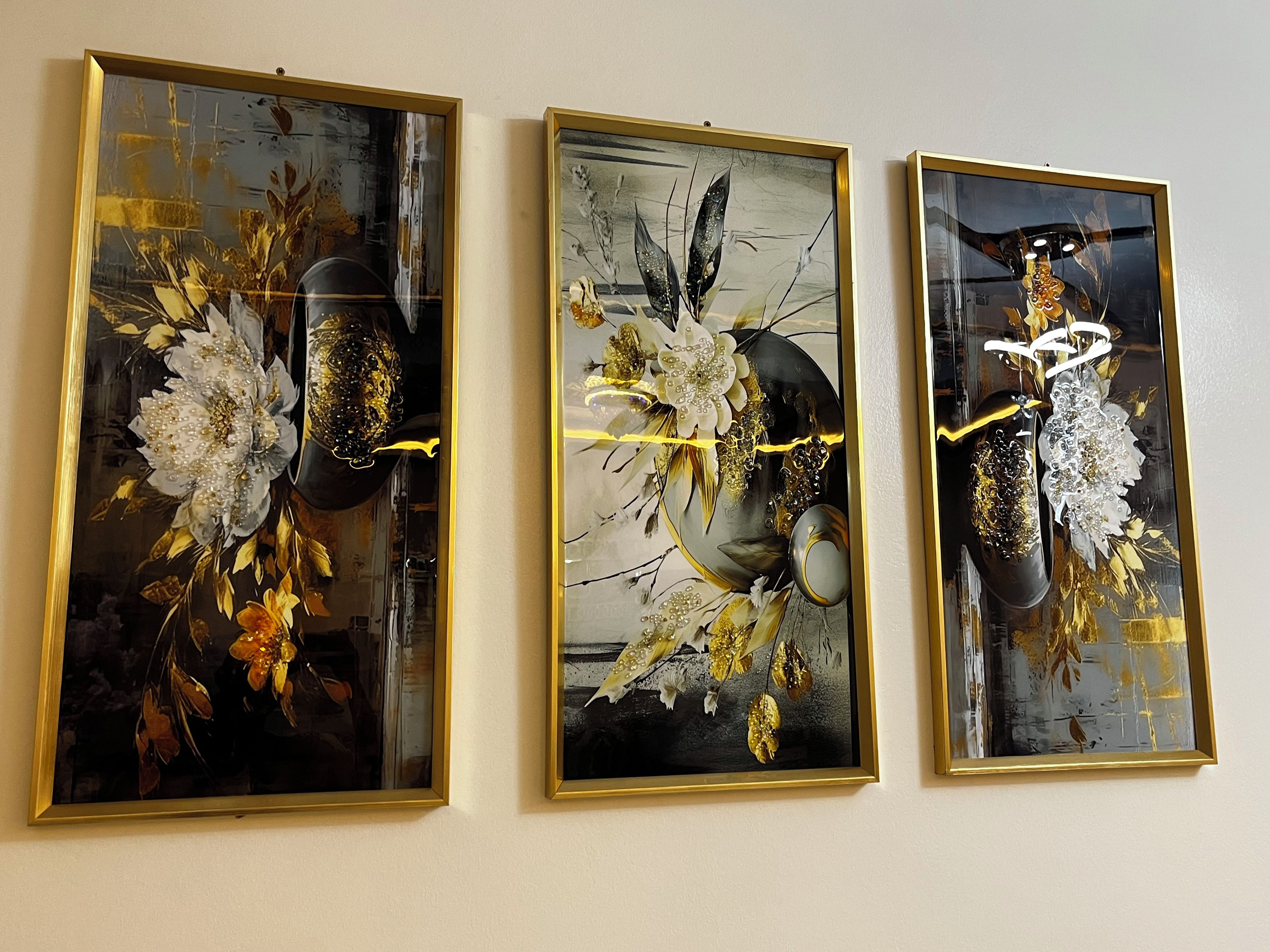Three framed artworks with floral and abstract designs, hung on a plain wall.