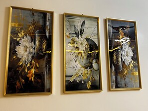 Tres obras de arte enmarcadas con diseños florales y abstractos, colgadas en una pared lisa.