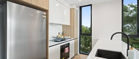 A modern kitchen with a stainless steel refrigerator, a built-in oven, and a large window providing a view of trees.
