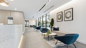 A modern reception area with a marble reception desk, seating area with sofas and chairs, and framed artwork on the walls. - The Serenity | New Riverview Apt + Pool & Parking (Surfers Paradise)