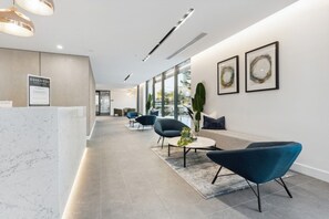 A modern reception area with a marble reception desk, seating area with sofas and chairs, and framed artwork on the walls. - The Serenity | New Riverview Apt + Pool & Parking (Surfers Paradise)