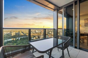 Ein Balkon mit einem Glastisch und Stühlen mit Blick auf eine Stadtlandschaft und einen Fluss.