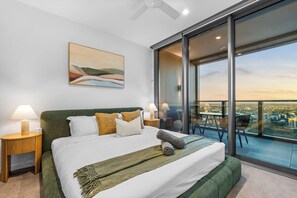 Een moderne slaapkamer met een groot bed, een balkon met uitzicht op de stad en een schilderij aan de muur.