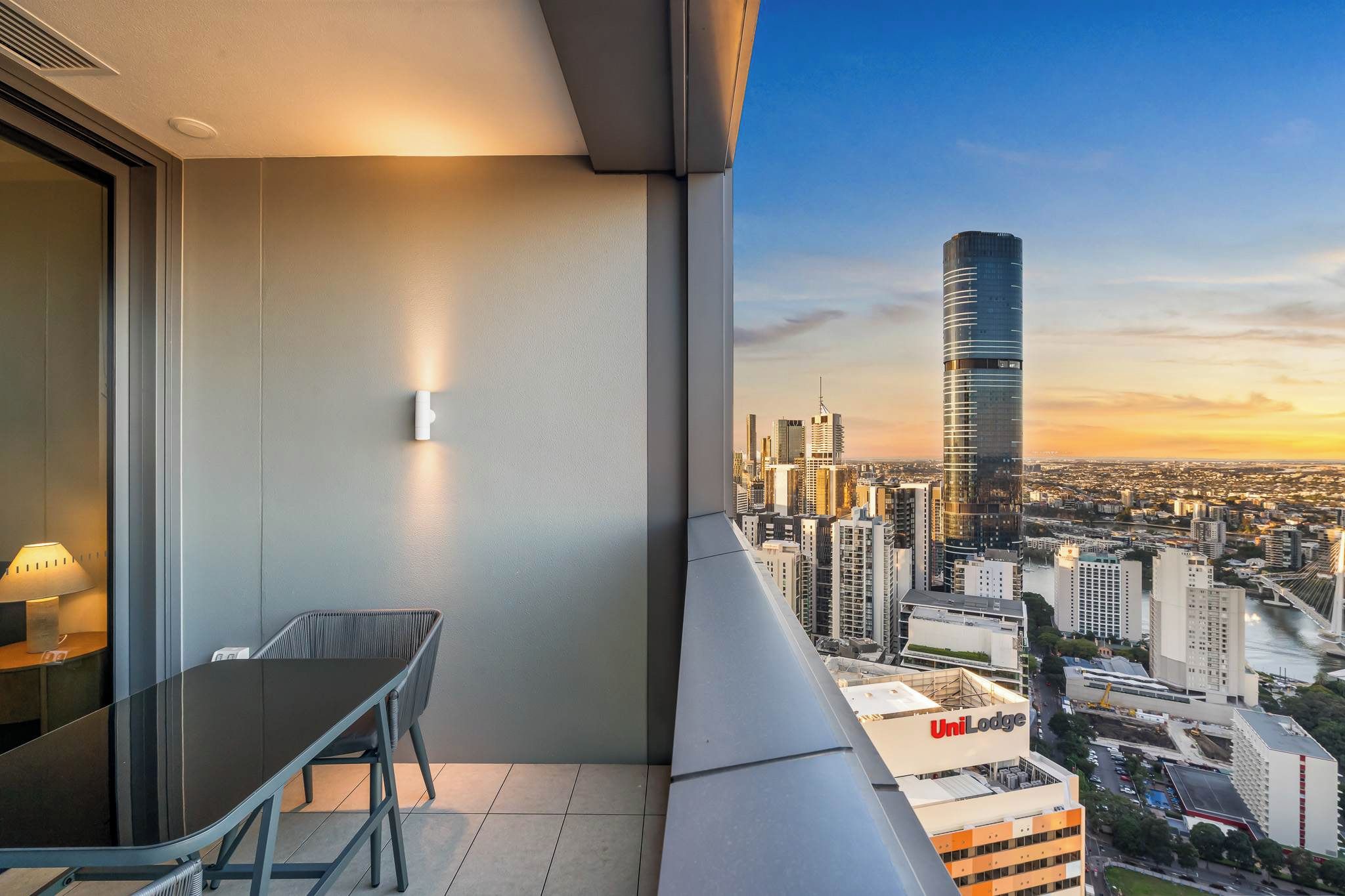 Un balcon avec une table et une chaise, une vue sur la ville avec un bâtiment UniLodge, et un gratte-ciel moderne.