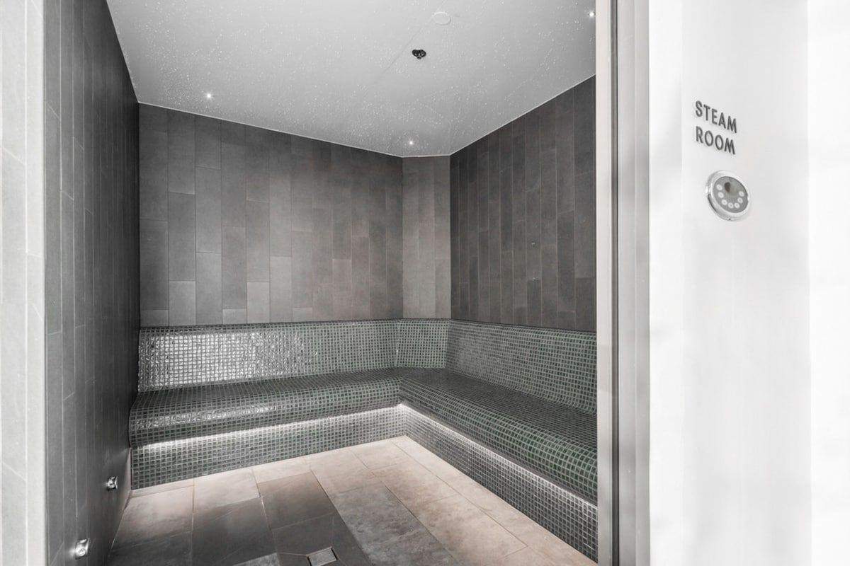 Un hammam avec un banc, des murs carrelés et un panneau de commande.
