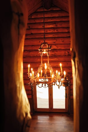 Un lustre orné de nombreuses bougies, dans une pièce en bois dont le plafond est en pente.