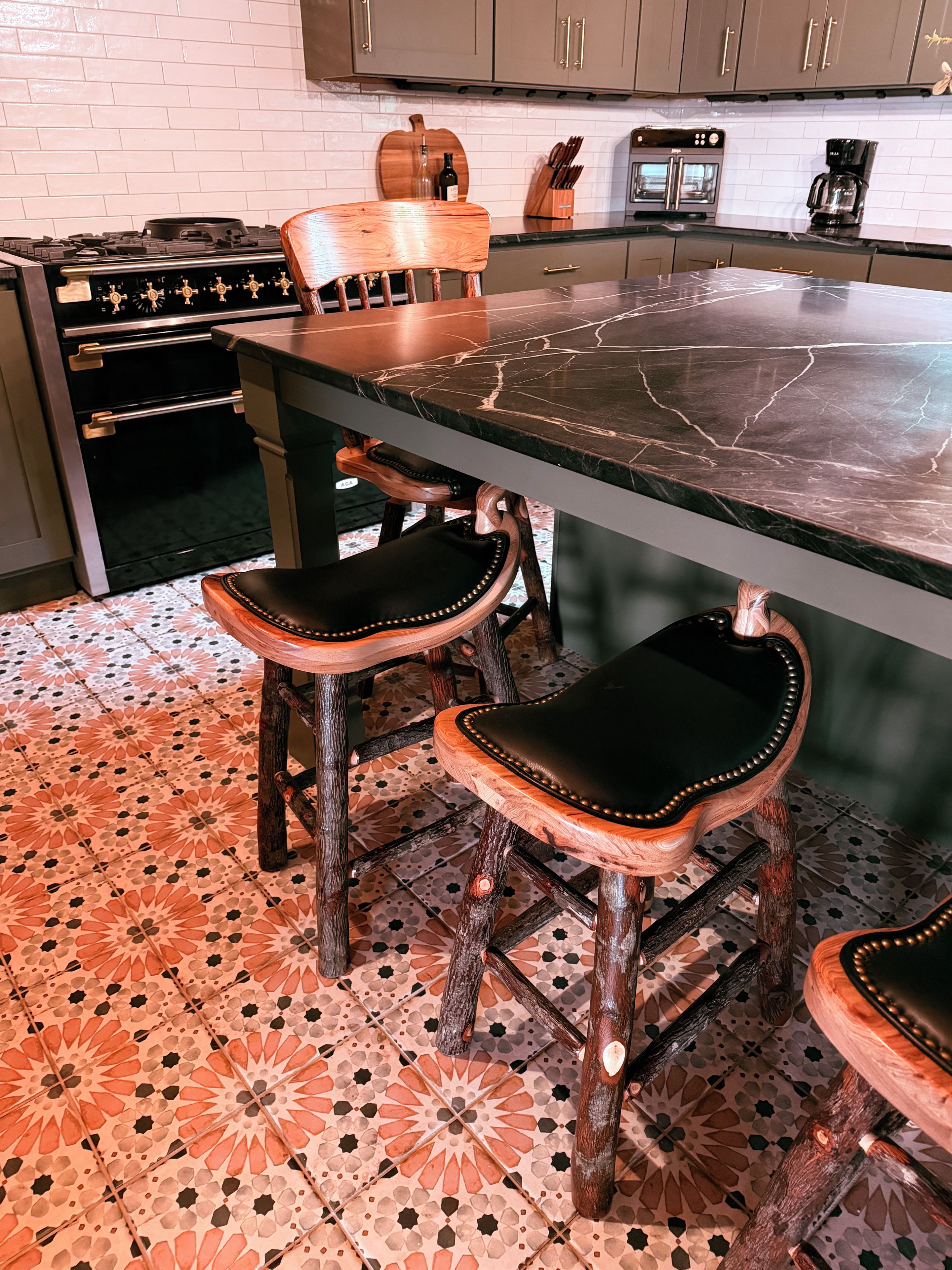 Une cuisine dotée d’un plan de travail en marbre, de chaises en bois avec des assises en cuir et d’un sol carrelé à motifs.