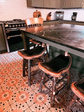 A kitchen with a marble countertop, wooden chairs with leather seats, and a patterned tile floor. - Peaceful Montana Ranch Getaway (Custer)