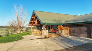A log cabin with a stone foundation, a green metal roof, and a garage. - Peaceful Montana Ranch Getaway (Custer)