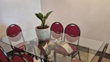 A glass-top table with six red chairs, a potted plant, and two framed pictures on the wall.