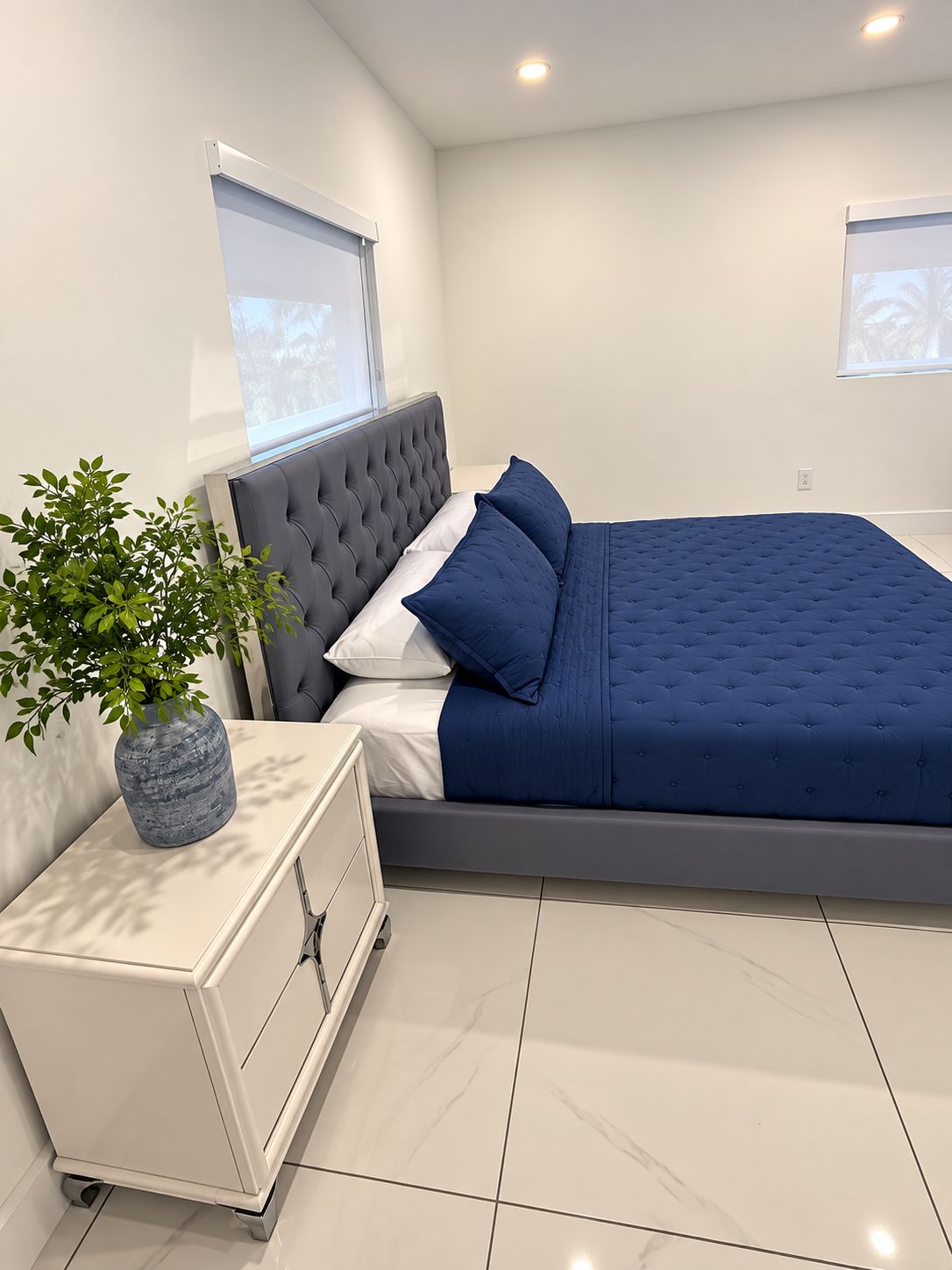 A modern bedroom with a bed, bedside table, and a potted plant.