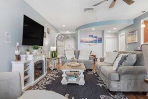A modern living room with a fireplace, grey sofas, a coffee table, and a flat-screen TV. - Sojourn 3BD2BA with Balcony, 3 Pools, Beach Access (Virginia Beach)