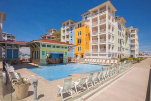 A hotel with a swimming pool, multiple balconies, and a clear sky. - Sojourn 3BD2BA with Balcony, 3 Pools, Beach Access (Virginia Beach)