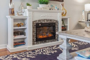 A fireplace with a stone surround, a mantel with decorative items, and a bookshelf with books. - Sojourn 3BD2BA with Balcony, 3 Pools, Beach Access (Virginia Beach)