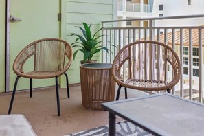 Een balkon met twee rieten stoelen, een klein rond tafeltje en een bloempot.