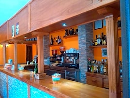 Una zona de bar con mostrador de madera, estanterías con botellas y una cafetera.