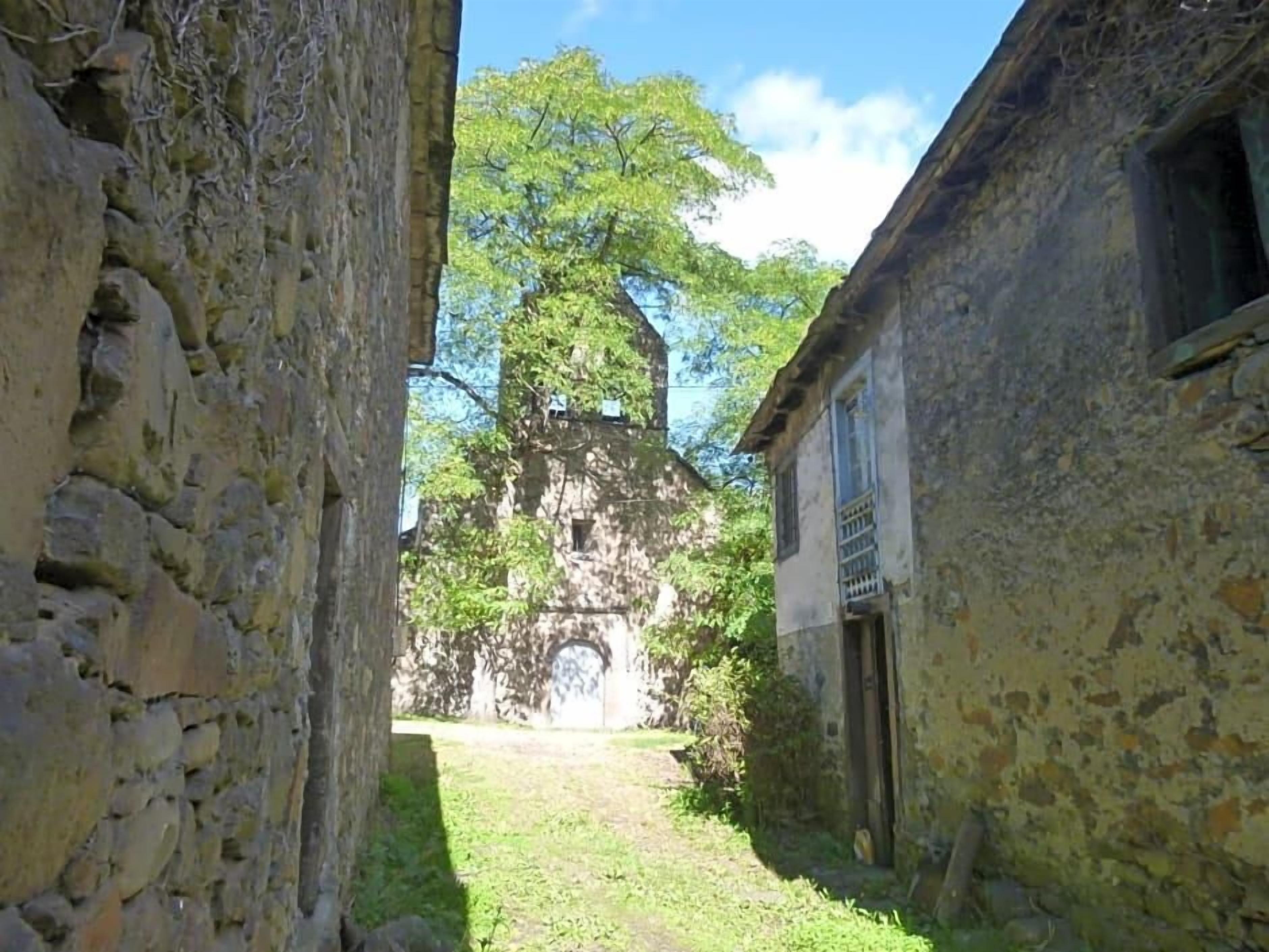 Ein schmaler Gang mit Steinwänden, ein Gebäude auf der rechten Seite und eine Kirche mit einem Glockenturm in der Ferne.
