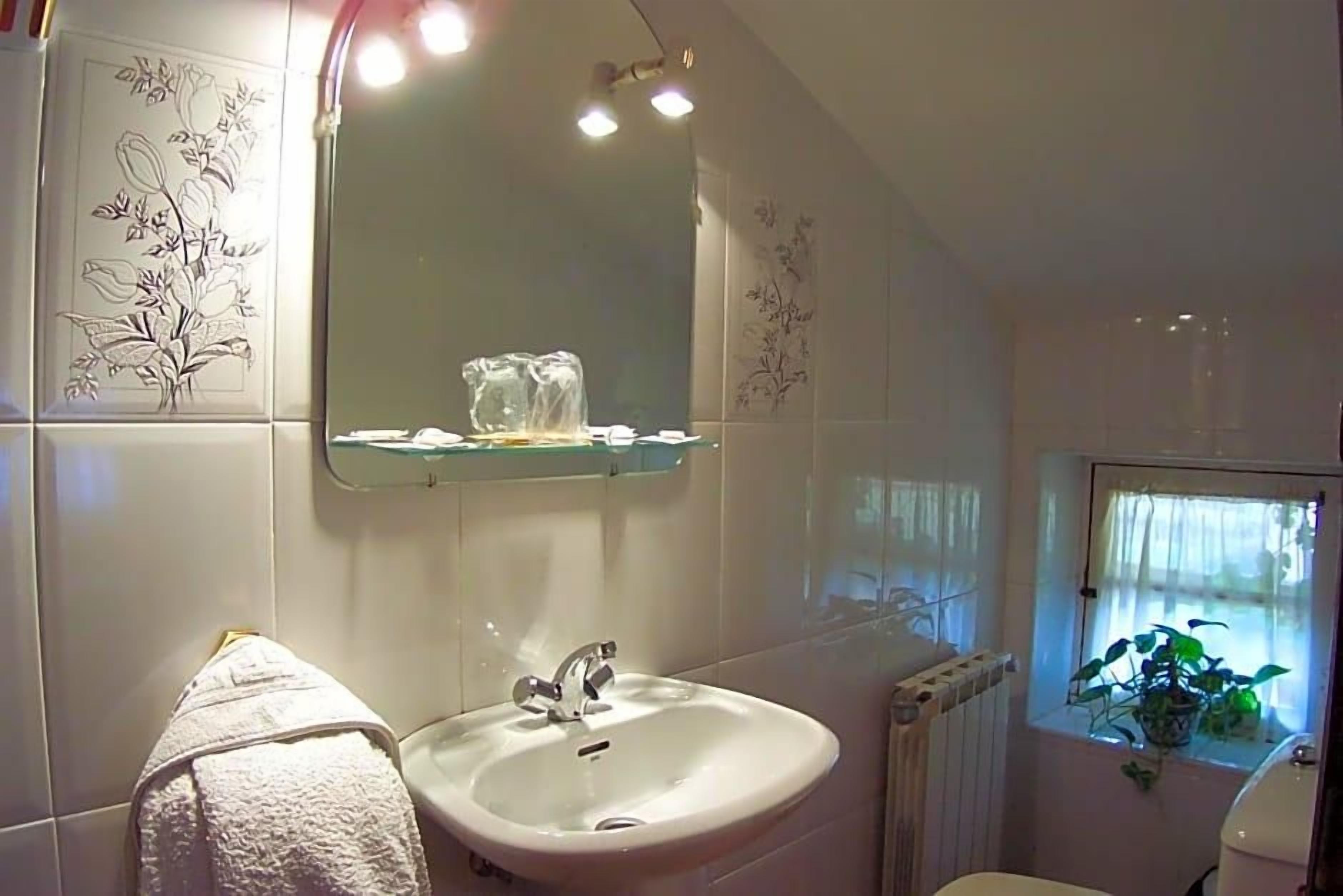Een badkamer met een witte wastafel, een spiegel en een raam met een plant.