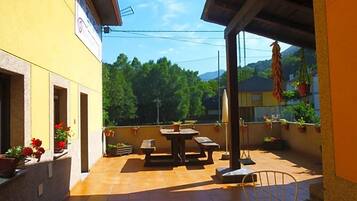 An outdoor patio area with a table and chairs, surrounded by potted plants and a yellow building facade.