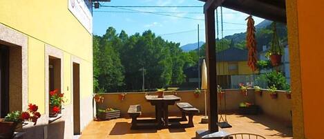 An outdoor patio area with a table and chairs, surrounded by potted plants and a yellow building facade.