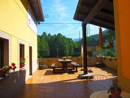 Un patio al aire libre con una mesa y sillas, rodeado de plantas en macetas y una fachada de edificio amarilla.