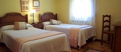 A hotel room with two beds, a nightstand, a lamp, a chair, and a window with curtains.