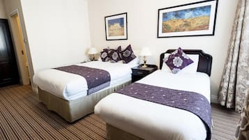 A hotel room with two beds, each with a pillow and a blanket, a nightstand with a lamp, and two framed paintings on the wall.