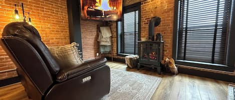 A cozy room with a leather recliner, a fireplace, and a large window with blinds.
