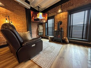 A cozy room with a leather recliner, a fireplace, and a large window with blinds.