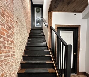 Eine Treppe mit dunklen Stufen und einem schwarzen Geländer, die zu einer Tür mit weißem Rahmen führt.