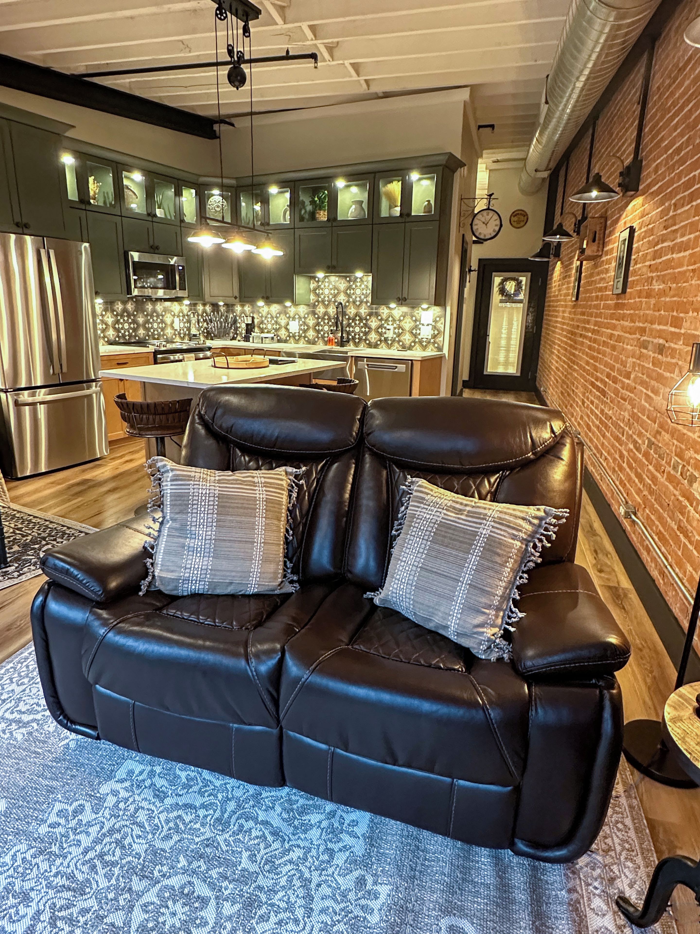 A modern living room with a leather sofa, a patterned rug, and a kitchen in the background.
