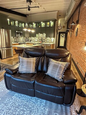 Ein modernes Wohnzimmer mit einer Ledersofa, einem gemusterten Teppich und einer Küche im Hintergrund.