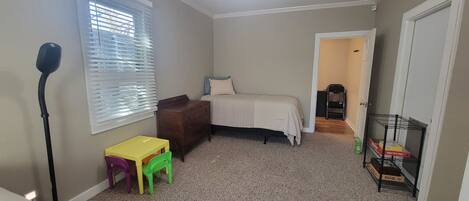 Een slaapkamer met een bed, een kaptafel, een bureau met stoelen, een radiator, een radiatoromsluiting, een deur en een plank met dozen.