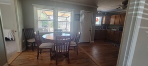 A dining area with a round table and four chairs, a kitchen with wooden cabinets, and a view through the window.