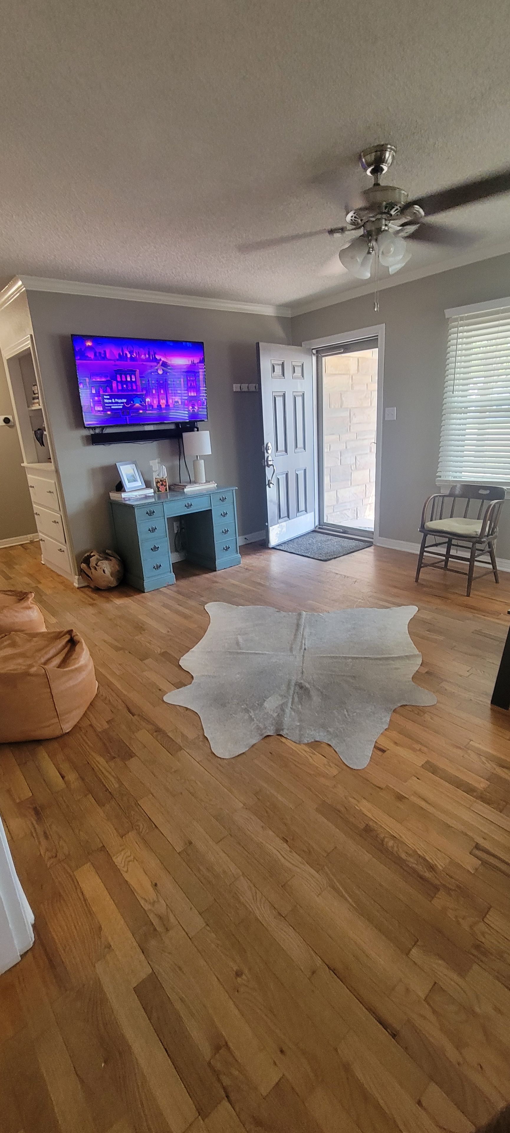 Una sala de estar con piso de madera, televisor, un mueble azul y una puerta que da al exterior.