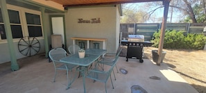 An outdoor patio with a table and chairs, a grill, and a wheelbarrow.