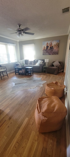 A living room with a wooden floor, a sofa, a coffee table, and a ceiling fan.