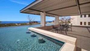 A clear blue infinity pool with a view of the ocean, a covered outdoor seating area with tables and chairs, and a modern architectural design. - Vista Añuiti: 2BR w/ Spectacular Ocean Views (Cabo San Lucas)