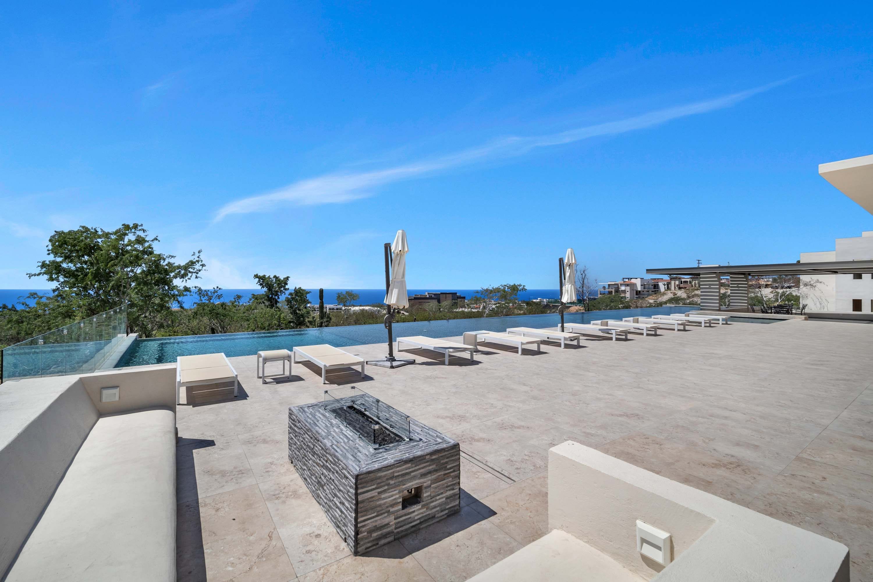 Un espace piscine aménagé sur le toit, avec des chaises longues et des parasols, offrant une vue sur une étendue d’eau.