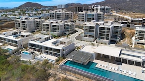 Un moderno complejo residencial con varios edificios de apartamentos, una piscina central y un paisaje montañoso al fondo.
