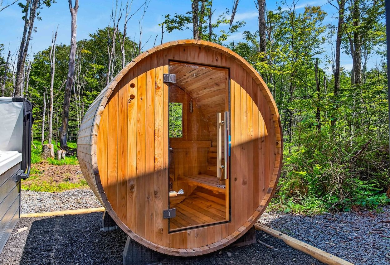 Une structure de sauna en bois, dotée d’une porte, située dans une zone boisée.